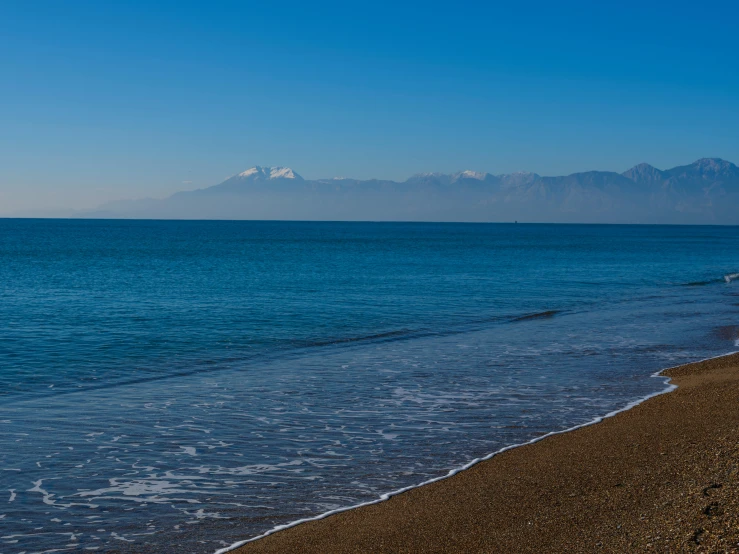 a beach area with blue water, mountains and a body of water