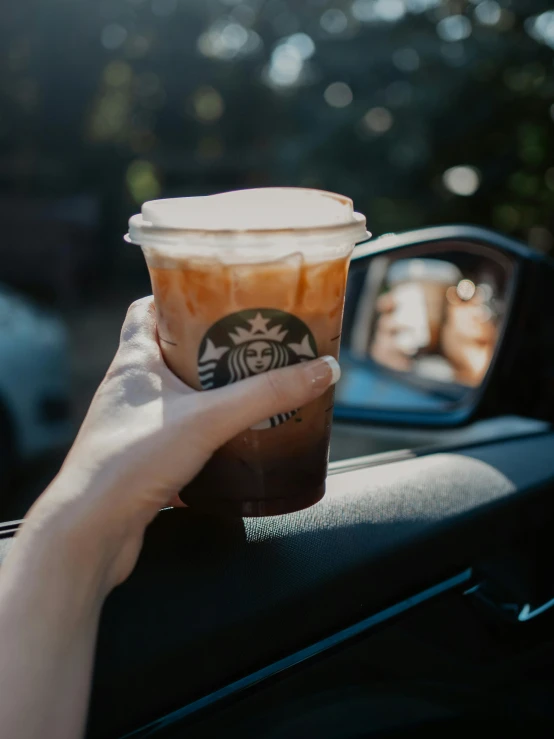 woman driving a car and holding up a starbucks cup