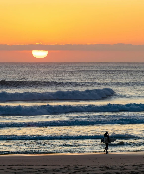 a surfer with a surfboard walking on the beach