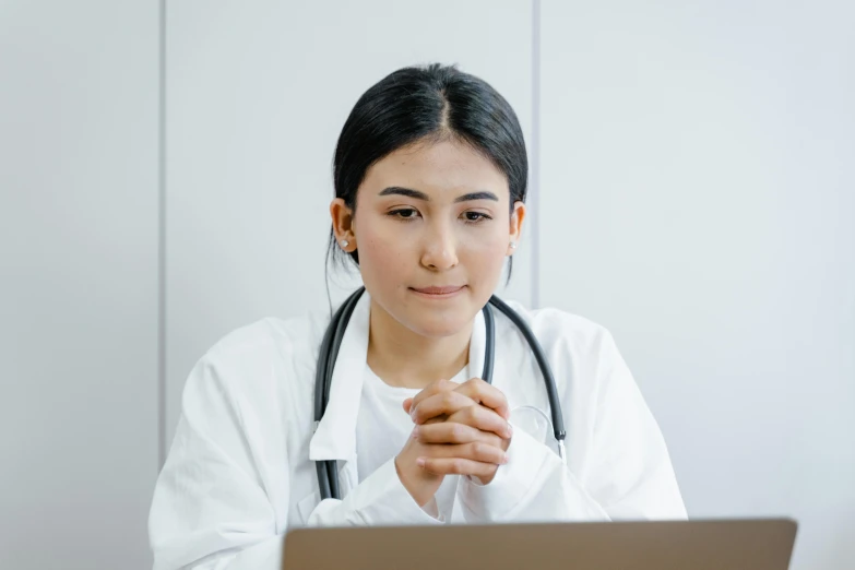 an asian woman in a white lab coat is looking at a computer