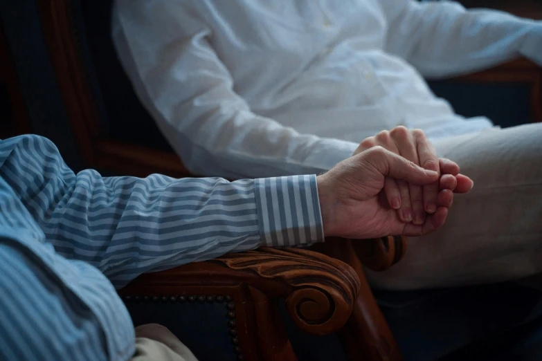 two men siting in wooden chairs holding hands