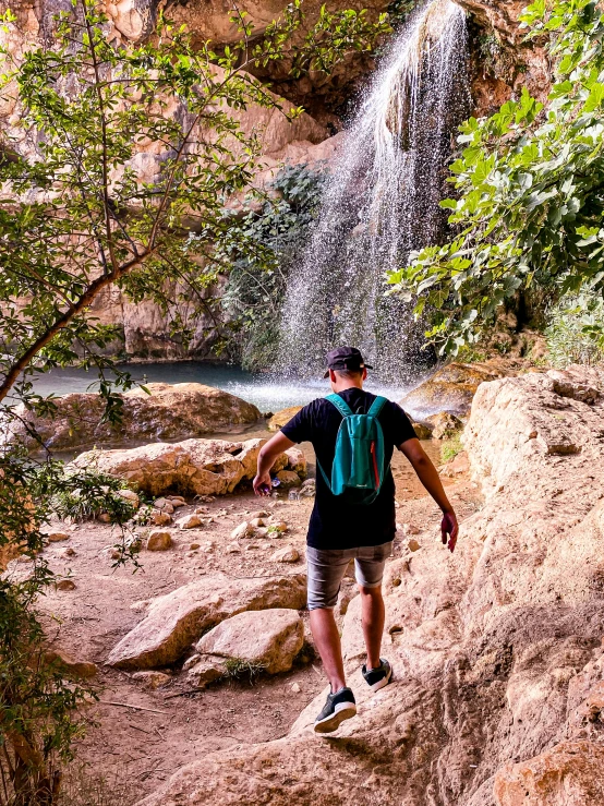 man wearing backpack approaching a waterfall in the mountains