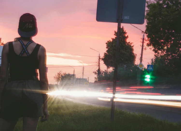 woman at a stoplight looking at a road with a car behind her