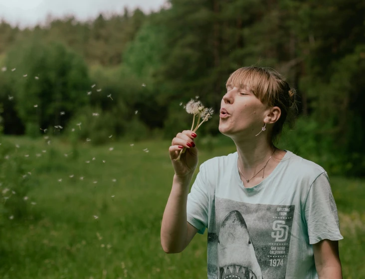 a woman blowing dandelion into the air while standing in a field