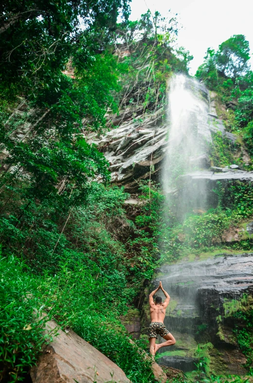 a shirtless man standing by the edge of a waterfall