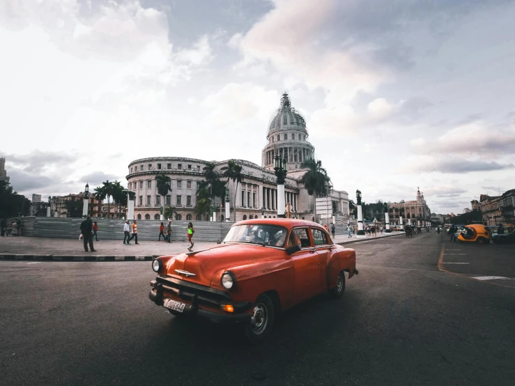 an orange car in the middle of a street in front of old buildings