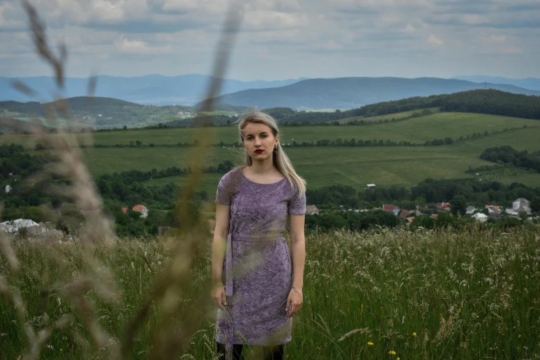 a young woman in purple dress standing on grass with mountains in the background