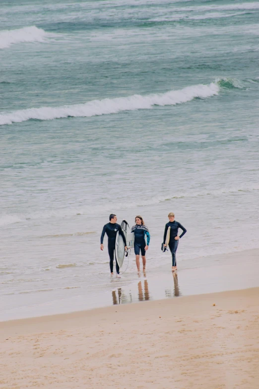 three people carrying surfboards on a beach by the water