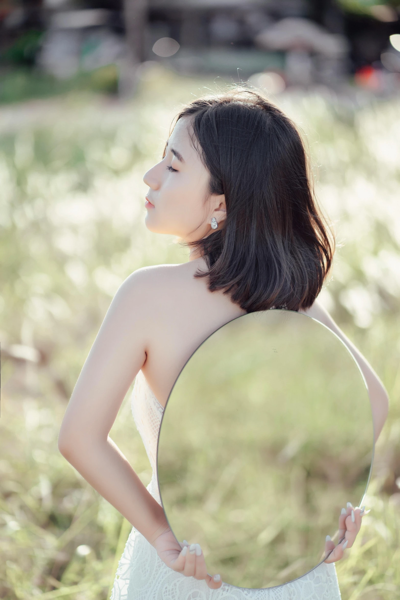 a woman standing in the grass looking through a mirror