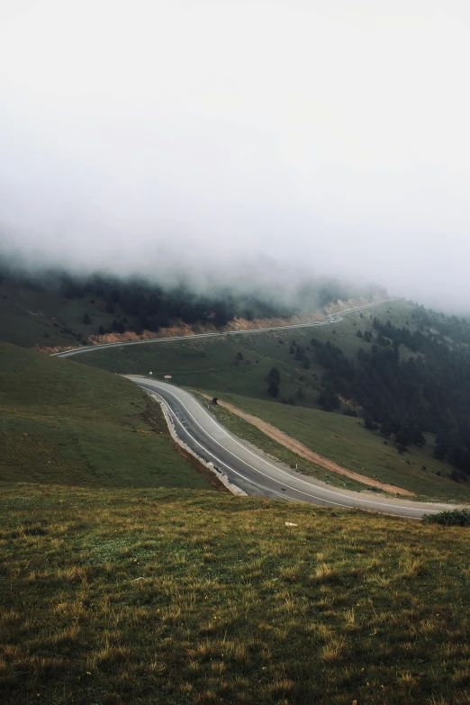 fog rolling over a hilly road with lush green grass