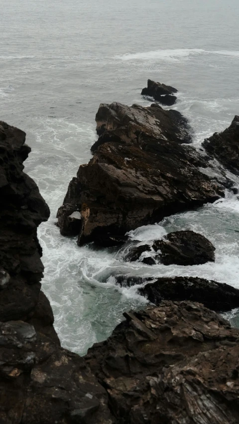 the ocean is moving down rocks on a foggy day