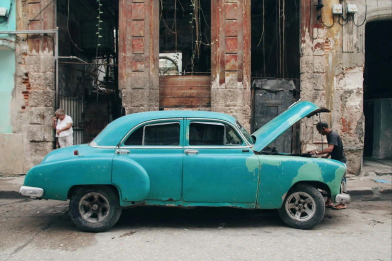 a man in black shirt looking into an old car with its hood open