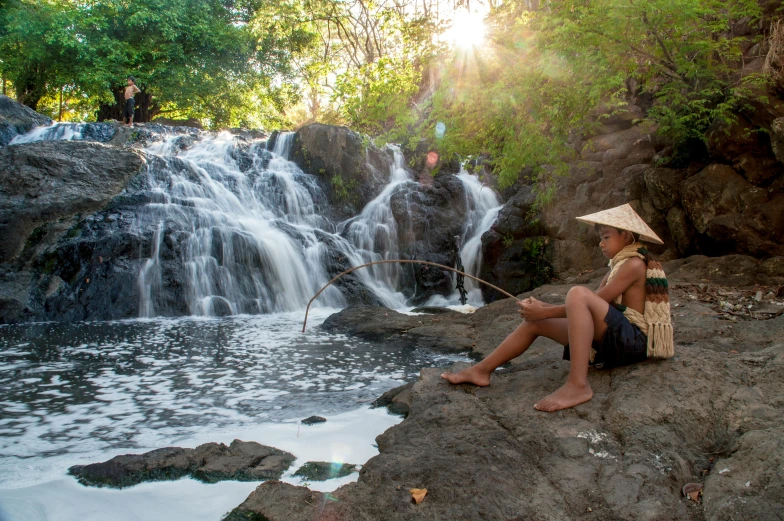 the woman is fishing at a waterfall near some rocks