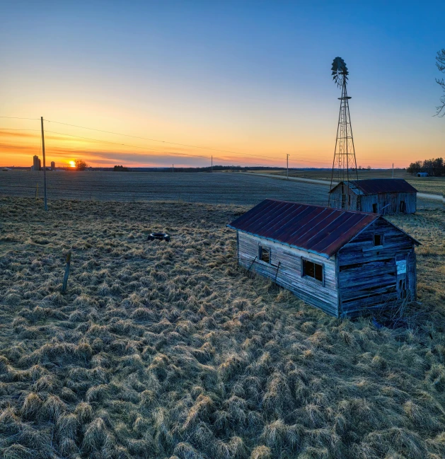 an old farm barn sitting in the middle of a field with a windmill and windmill wheel