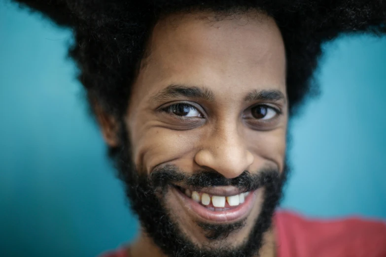 a man with an afro and blue background smiles