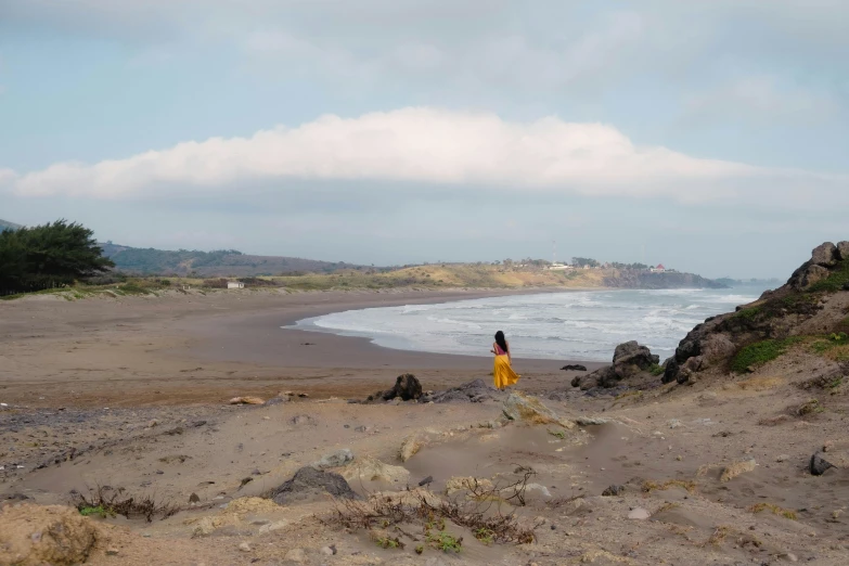 a woman in a yellow dress on the beach by the water