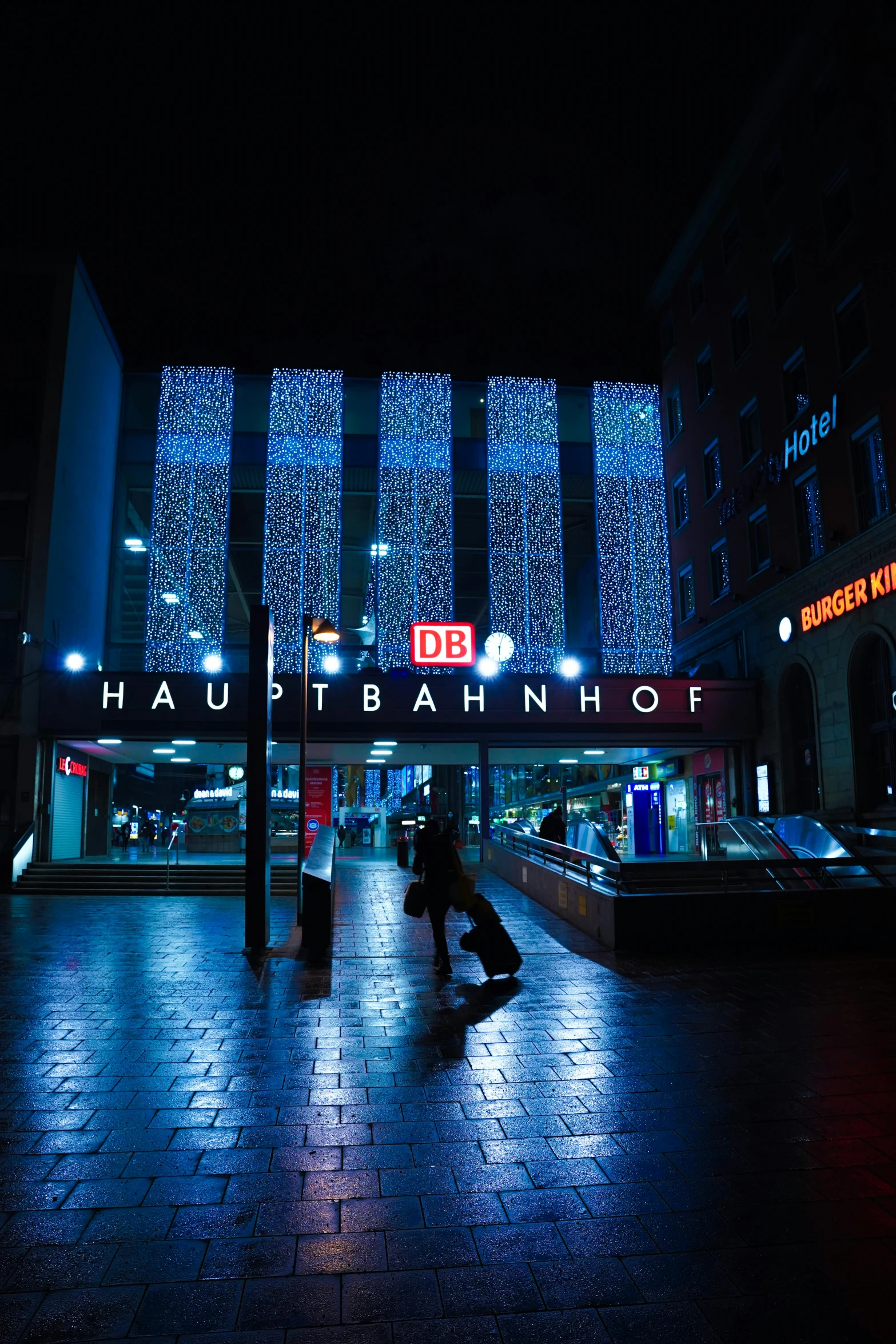 people walk in a plaza at night with lights on the building