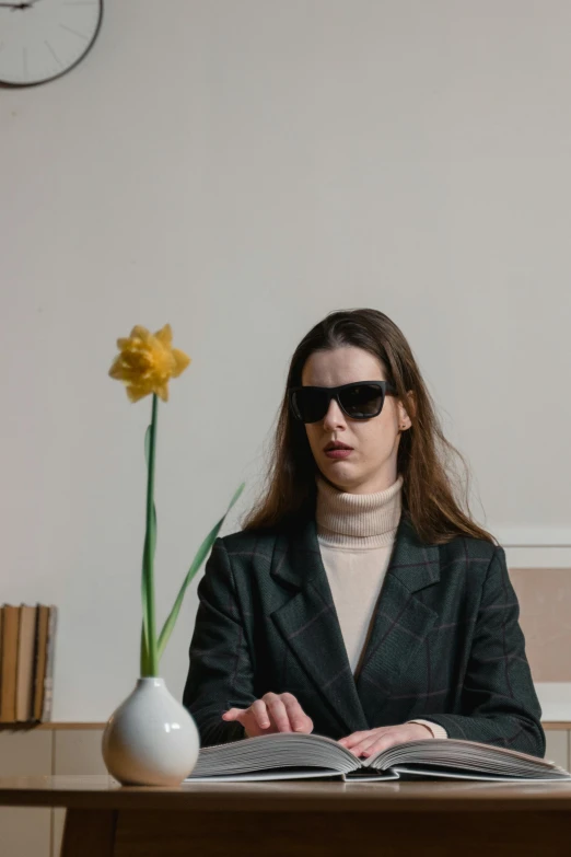 a woman in black jacket wearing sunglasses sitting at desk