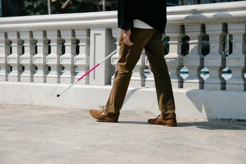 a person wearing brown pants and shoes walking with a pink walking stick