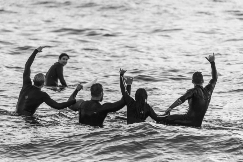 five surfers stand in the water and wave their hands in the air