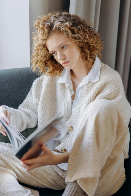 a woman sits on a couch and holds a magazine