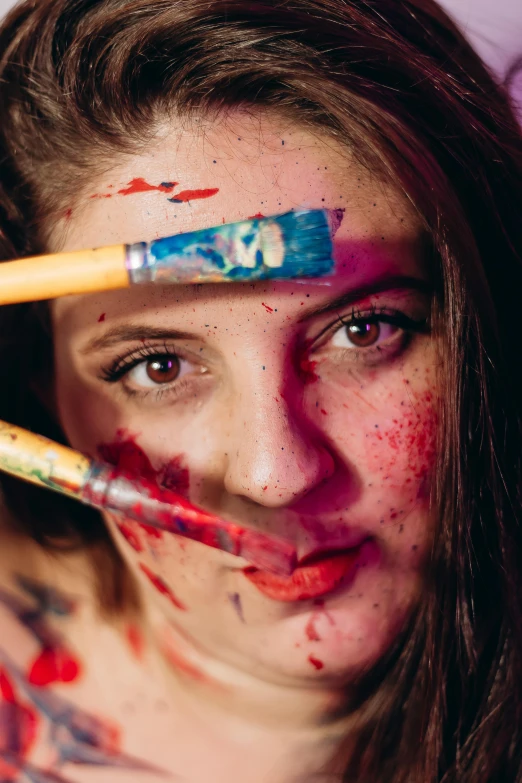 a girl with paint smeared on her face holding two brushes