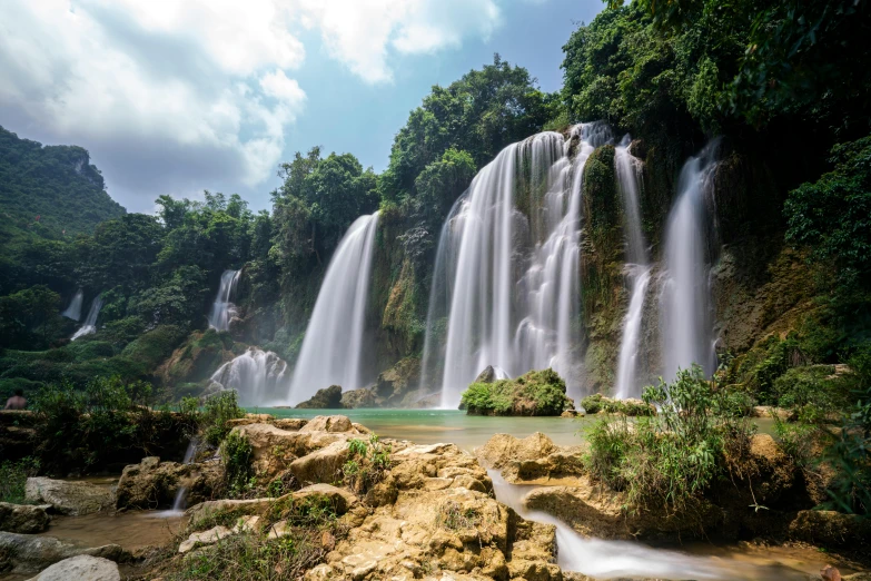 many tall waterfalls pouring into a river near rocks