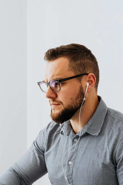 a man in a gray shirt with glasses has earphones on his ears