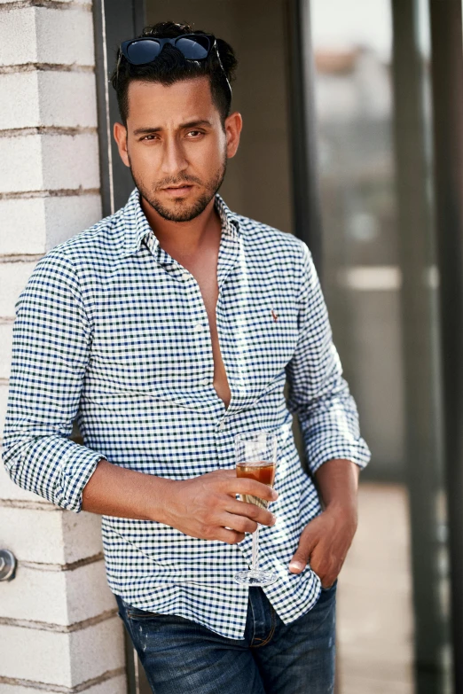 a man leans against a wall in a plaid shirt and jeans