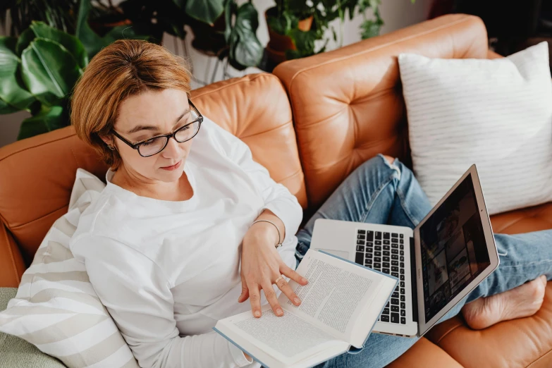 a woman sits on a leather couch while looking at her laptop computer