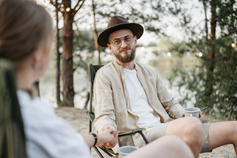 a man with glasses on his face sits next to a woman who is holding coffee cups