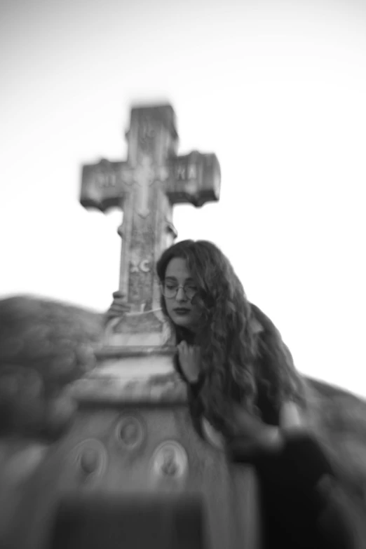 a black and white po of a woman sitting in front of a cross