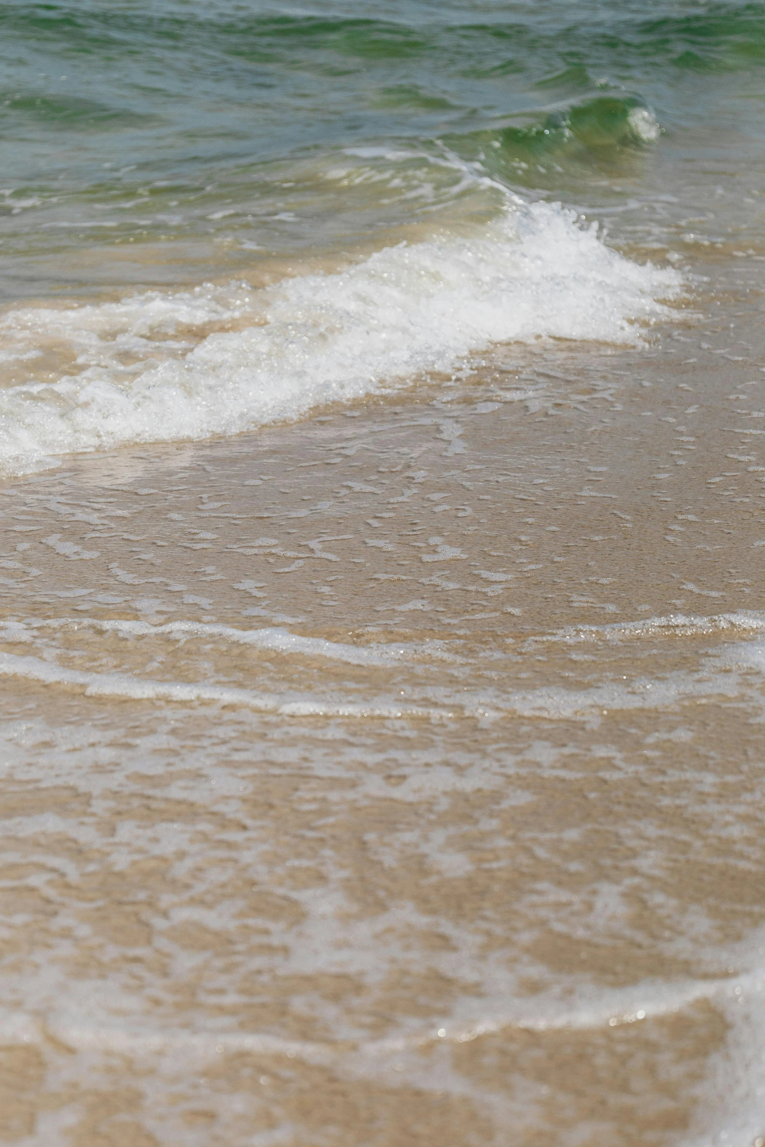 a sandy beach with waves coming in and ocean sprays