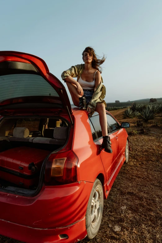 a girl sits on the back of a car, holding her head in her hand