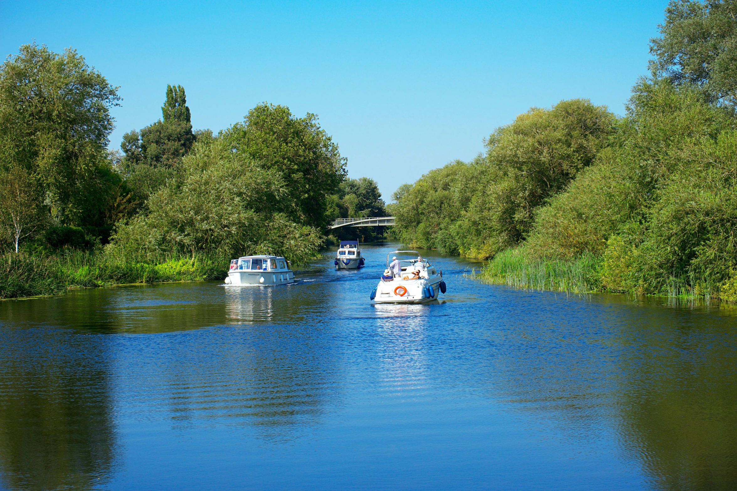 small boats sail down a large, shaded river