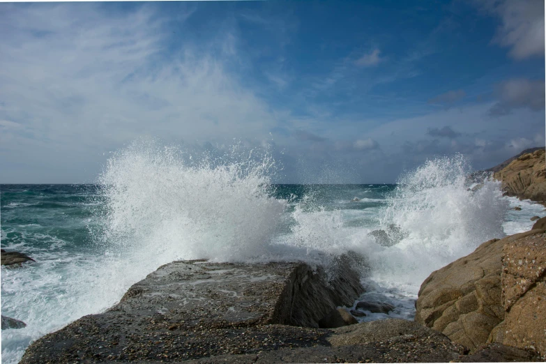 a rough wave breaks into the rocks at the beach