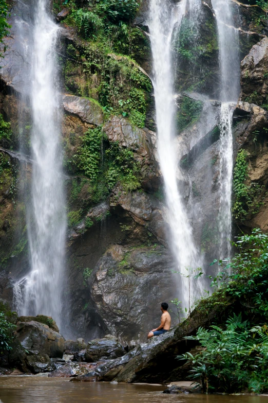 a man sits in the shade under a waterfall