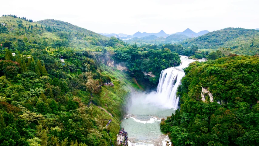 several people hiking in the green landscape and around the falls