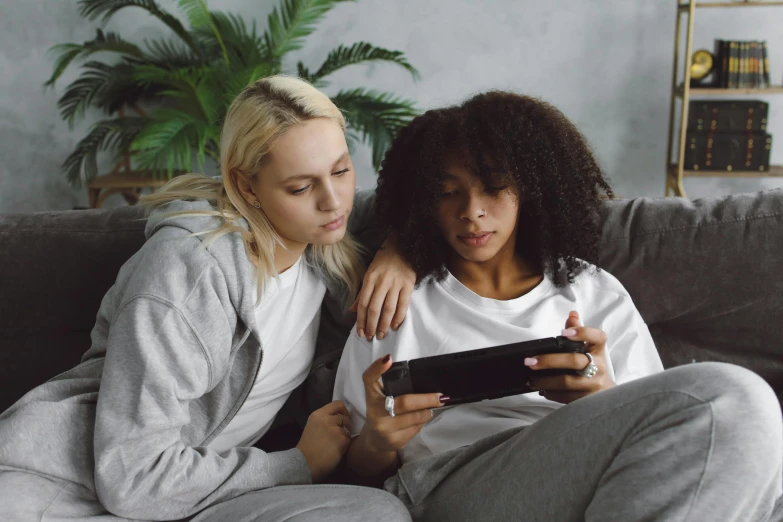 two women are sitting on a couch and looking at a tablet