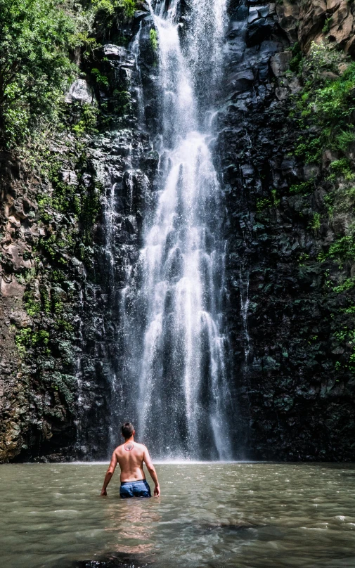 a man wades in the water at a waterfall