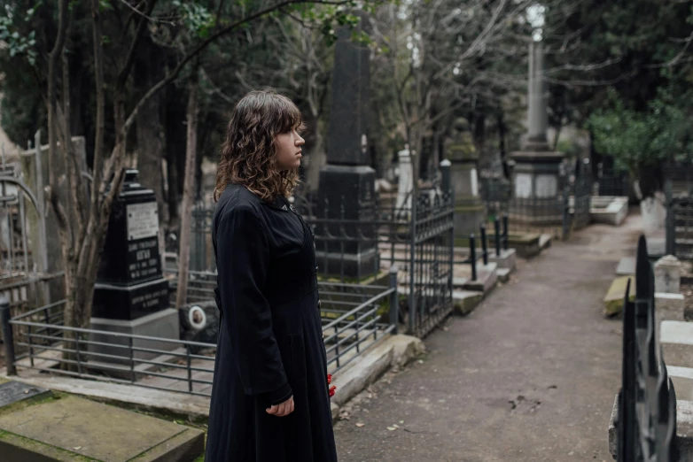 the woman is standing in a cemetery, staring away