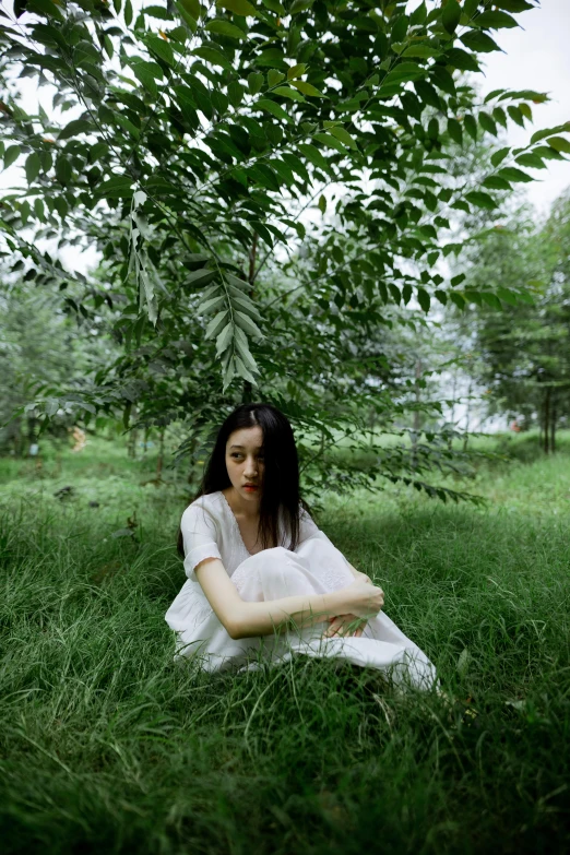 a young lady sitting in a field looking at soing