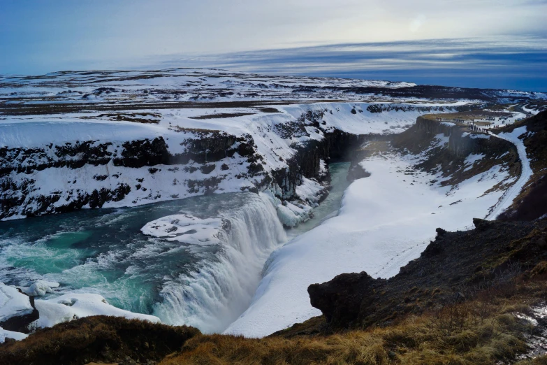 a waterfall covered in snow and surrounded by tall mountains