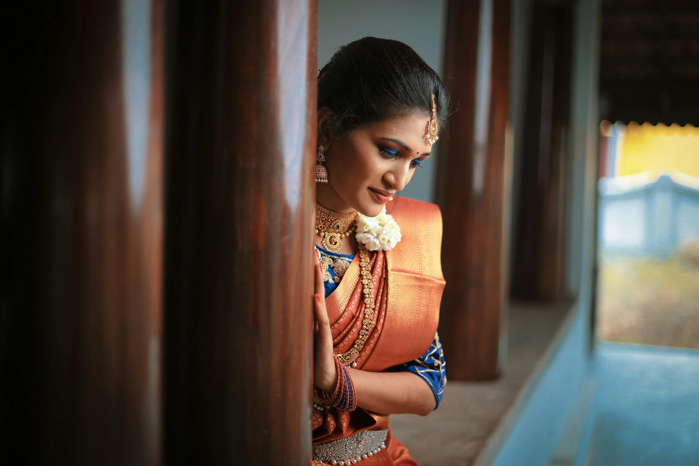 a woman looks at her jewelry from behind wooden pillars