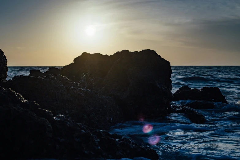 a sun sets over the ocean as seen from rocks