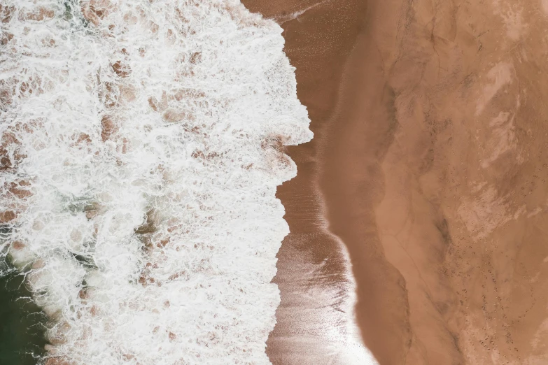 an aerial view of the ocean with a wave crashing into the shore