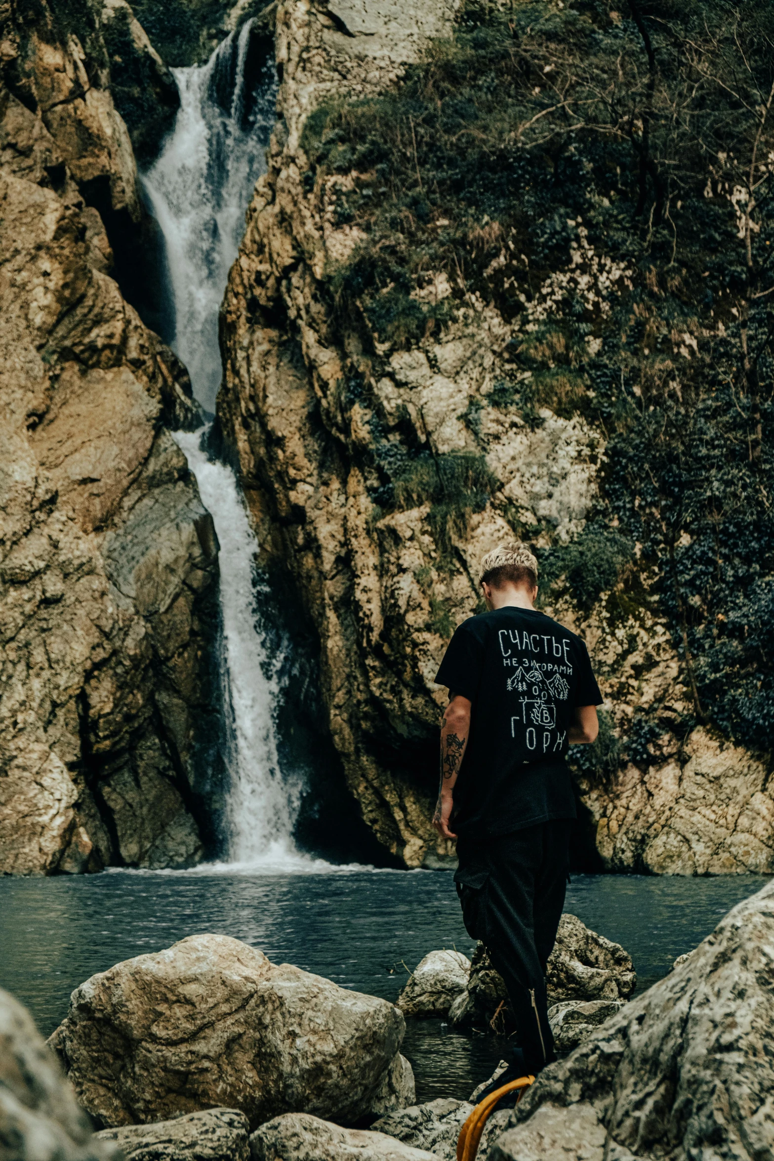 a man walking near a waterfall on top of a rock covered ground