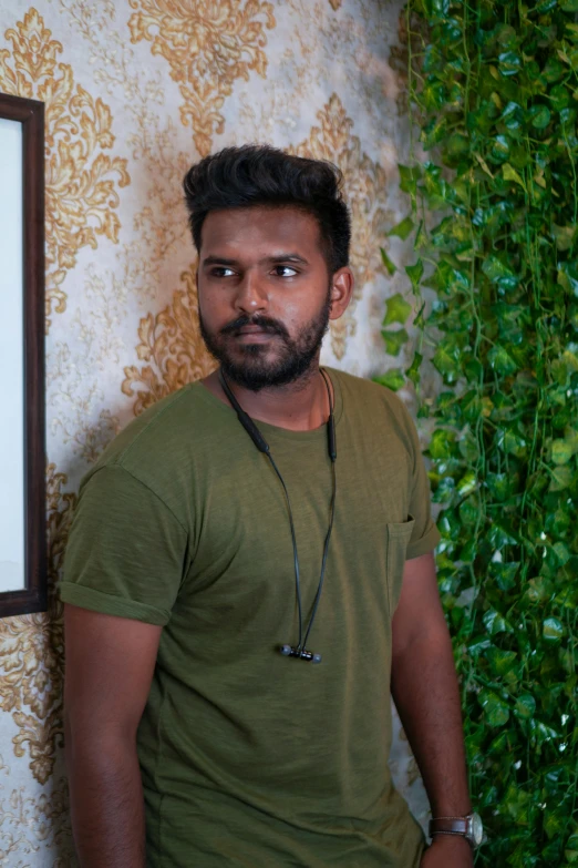 a man wearing a green t - shirt stands in front of a green wallpapered background