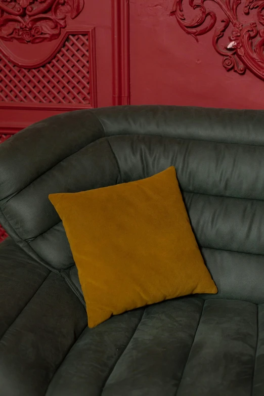 a yellow pillow on a gray couch against a red wall