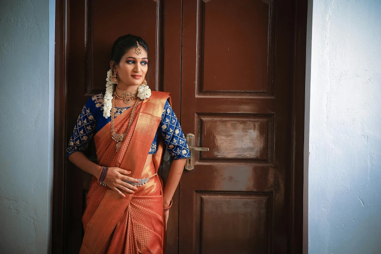 an indian woman in an orange dress standing against the door